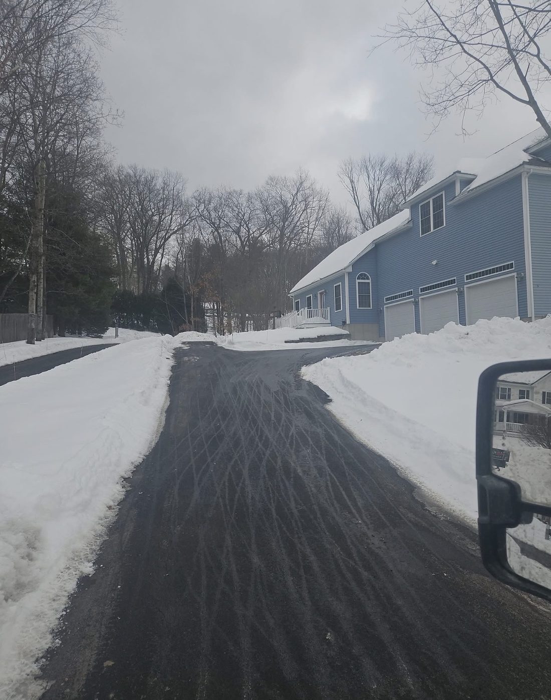 A residential driveway cleared down its full width beside a home, with plowed snowbanks stacked back along both edges after service