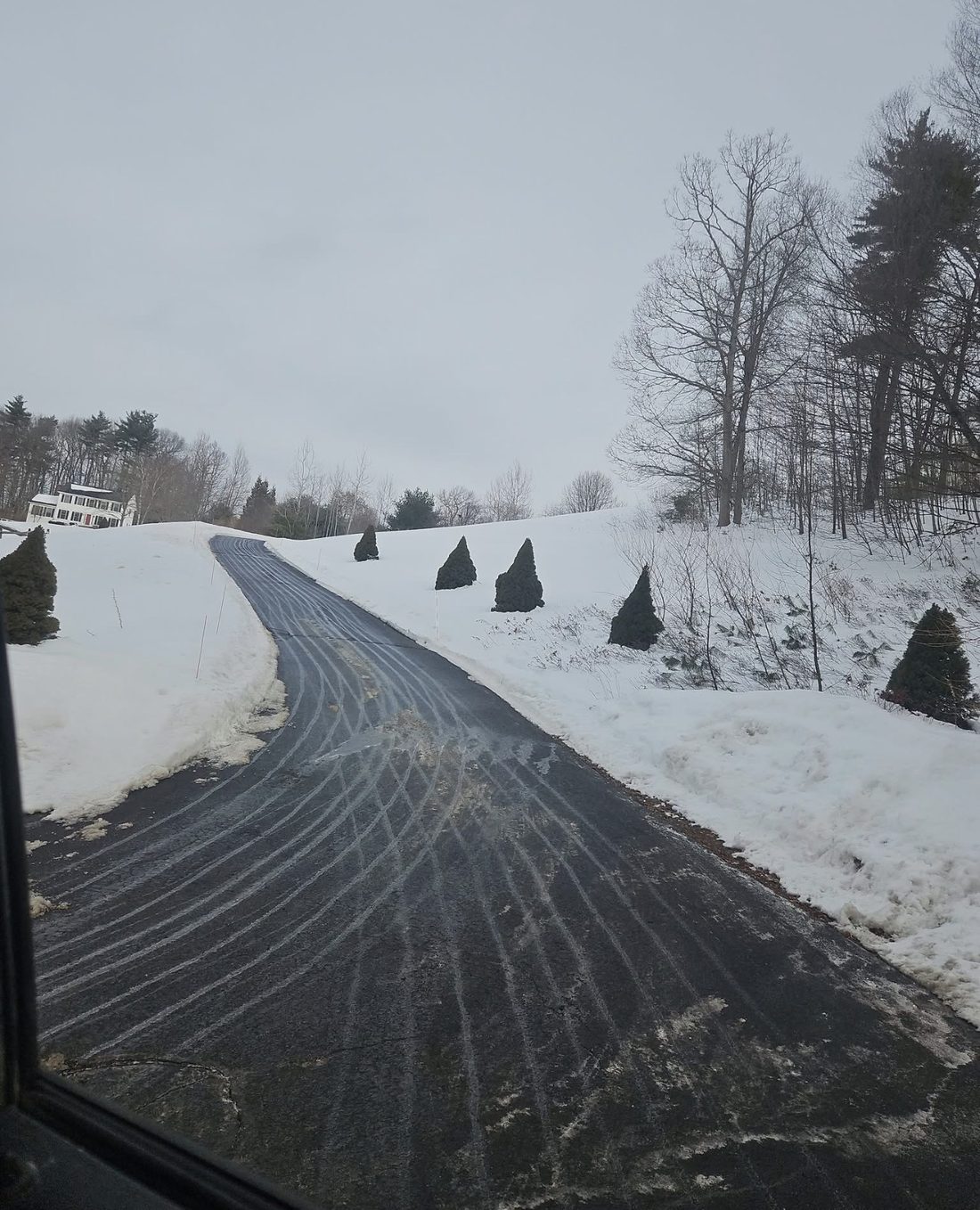 A long country driveway cleared up a hill toward a house, with snow banked off to the sides after a completed plow visit